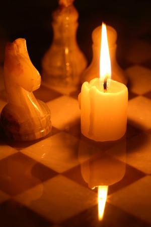 Set of chess pieces made from onyx against lighting candle on chessboardの写真素材