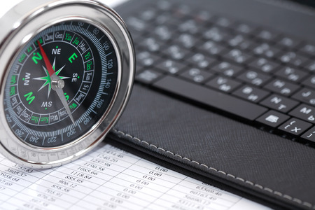 Business direction. Closeup of compass near laptop on paper with digits