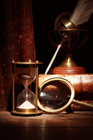 Vintage still life. Magnifying glass near hourglass on background with old bookの写真素材