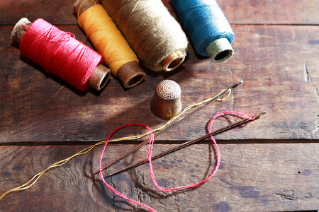 Thimble and needles near thread on old wooden background