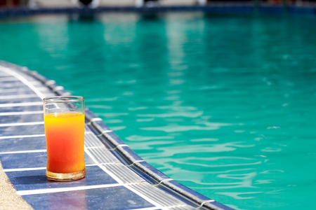 Closeup of orange juice glass standing on border of water poolの写真素材