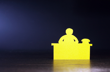Paper man bureaucrat sitting on table against dark backgroundの写真素材
