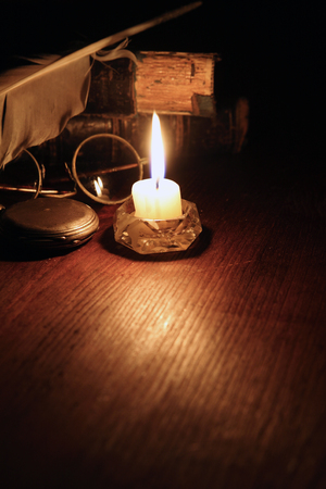 Vintage still life with quill pen and spectacles on old books near lighting candleの写真素材