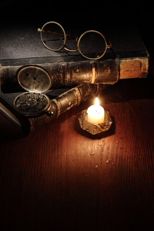 Vintage still life with quill pen and spectacles on old books near lighting candleの写真素材