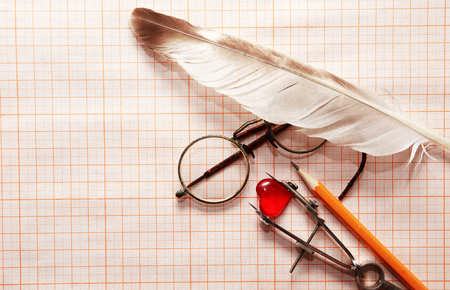 Old spectacles and measuring tools around red glass heart on graph paperの写真素材