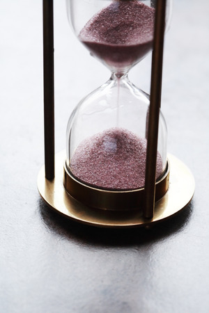 Vintage hourglass with flowing sand on dark backgroundの写真素材