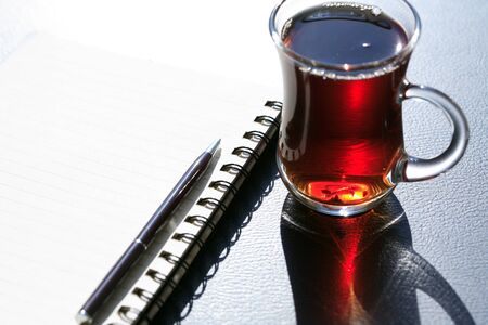 Pen on open spiral notepad with blank page near cup of teaの写真素材