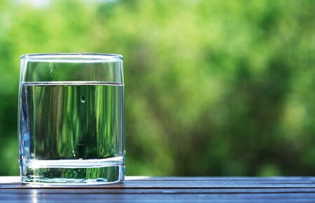 Glass of cold water against nice green nature backgroundの写真素材