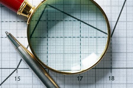 Closeup of magnifying glass near pen on paper background with graphの写真素材