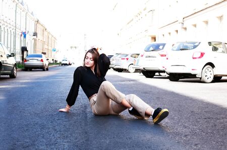 Beautiful young woman sitting on the roadway in the cityの写真素材