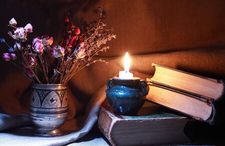 Vintage still life with bouquet of dried flowers in a silver vase near old book