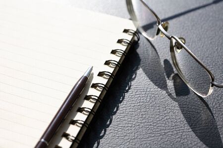 Pen on spiral notebook near spectacles on black tableの写真素材