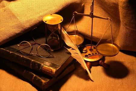 Old books and quill pen near hourglass on canvas backgroundの写真素材