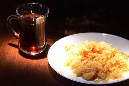 White plate with pilaf near cup of tea on wooden tableの写真素材