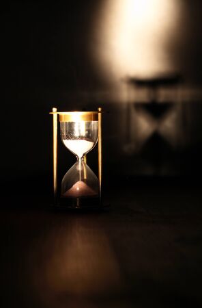 Vintage hourglass on wooden table against dark background with shadowの写真素材