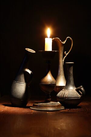 Set of nice ancient vases near lighting candle on dark backgroundの写真素材