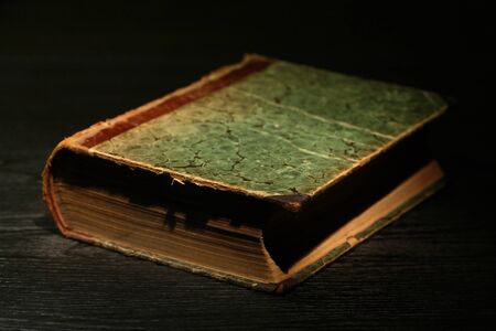 Very old book on black table under beam of lightの写真素材