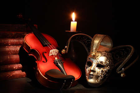 Nice violin near Venetian mask and candle against black background