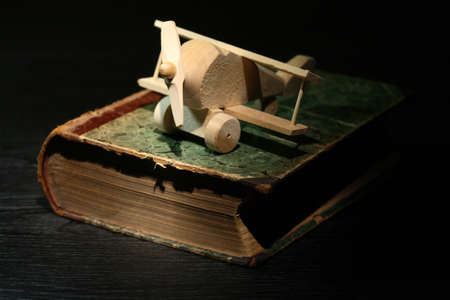 Education concept. Small wooden airplane on old book against dark backgroundの写真素材