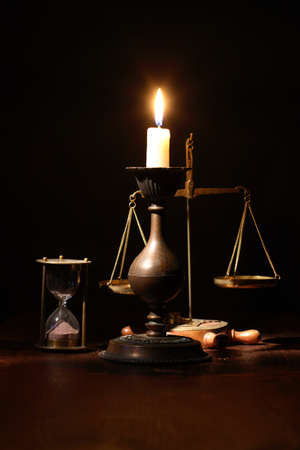 Elegant brass candlestick with lighting candle near hourglass and weight scaleの写真素材