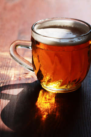 Mug of beer with foam on wooden table under sunlightの写真素材