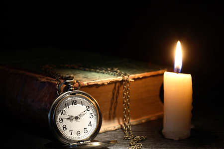 Old pocket watch near old book and candle on dark backgroundの写真素材