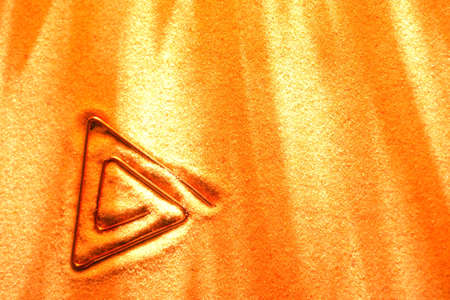 Abstract triangular symbol made from copper wire on sand surfaceの写真素材