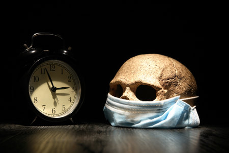 Covid concept. Human skull in medical mask near alarm clock