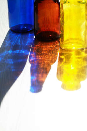 Set of empty multicolored glass bottles with nice shadow against sun lightの写真素材