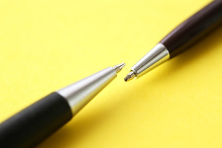 Two pens opposite each other on yellow paper backgroundの写真素材
