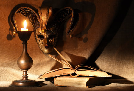 Nice old Venetian mask near lighting candle on canvas backgroundの写真素材