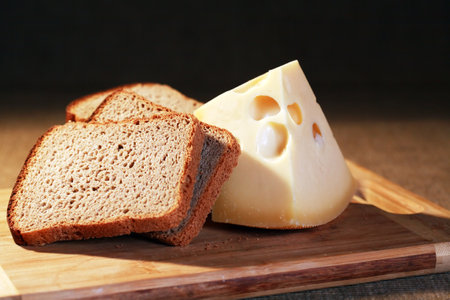 Cheese near bread on wooden board against dark backgroundの写真素材