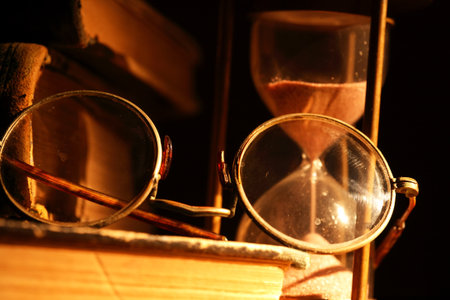 Vintage still life. Old glasses closeup on book near hourglassの写真素材