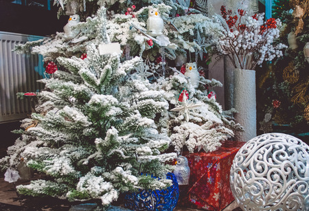 Small Christmas tree decorated with snow. White owl and figured sphere near. Big Christmas trees with garland lights on background.の写真素材