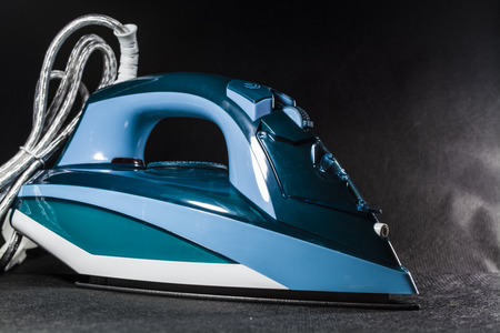 The blue iron for ironing of clothes. Monophonic black background. Household appliances. Electronics.の写真素材