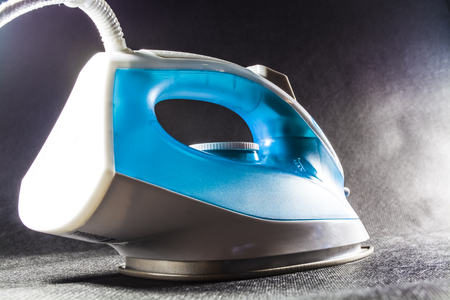 The blue iron for ironing of clothes. Monophonic black background. Household appliances. Electronics.の写真素材