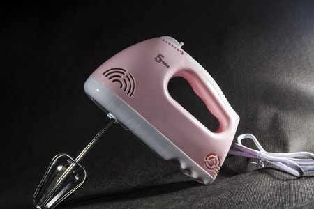 Home electric mixer of pink and white colors. On a monophonic black background. Nozzles for the mixer. Modern technologies. Equipment.の写真素材