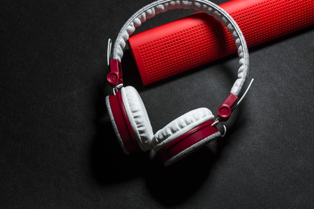 Big portable and multi-colored earphones and red column for listening of music. White and red color. On a monophonic black background. The place for an inscription.の写真素材