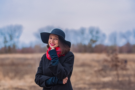 The girl in a black coat, a shovel hat and with red lipstick on lips, walks in the park. Style and modern fashionの写真素材