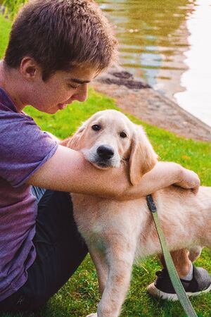 The young man walks with the little dog in the park. Golden retrieverの写真素材