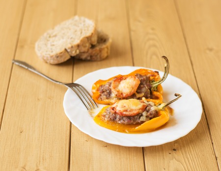 Baked pepper with meat, cheese and tomato on the plate on a wooden table. Home kitchen.の写真素材