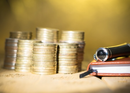 Metal coins with a notebook and fountain pen on a rustic table. Accessories for the business. Selective focus.の写真素材