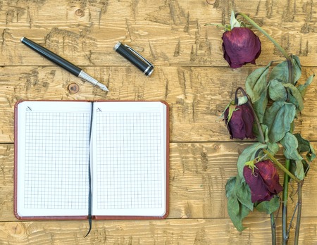 Wilted roses with a notebook and fountain pen on a rustic table. Concept of holiday memories. Top view.の写真素材