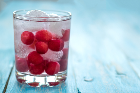 Cold water with ice, cherries and berries. Vintage background. A refreshing drink for a healthy diet.の写真素材