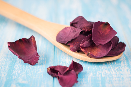 Dried rose petals in a wooden spoon on a rustic table. Component for herbal flavored tea. Selective focus.の写真素材