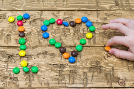Hands girls laid out colored candies on the table. Heart made of multi-colored candies. The concept of happiness and love.の写真素材