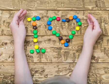 Hands girls laid out colored candies on the table. Heart made of multi-colored candies. The concept of happiness and love.の写真素材