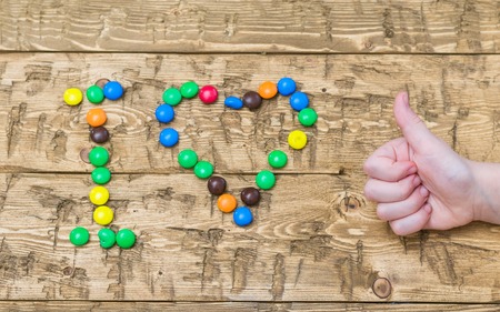 Hands girls laid out colored candies on the table. Heart made of multi-colored candies. The concept of happiness and love.の写真素材