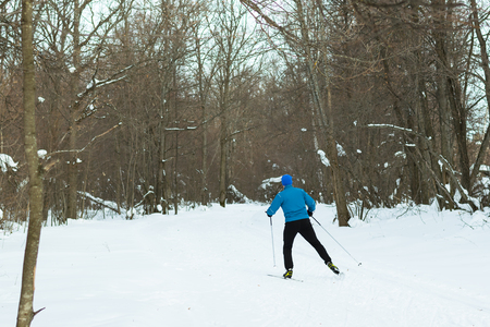 Man in a blue suit runs on skis in the winter woods. Ice ridge course skiing. Healthy lifestyle concept.の写真素材
