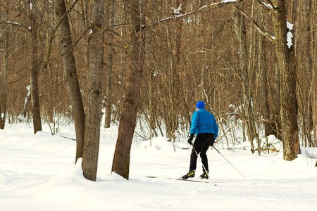 Man in a blue suit runs on skis in the winter woods. Ice ridge course skiing. Healthy lifestyle concept.の写真素材